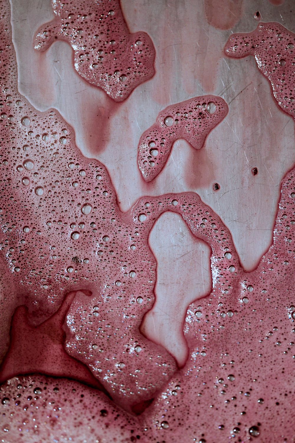 Close-up on wine and foam as wine drains from stainless vat.