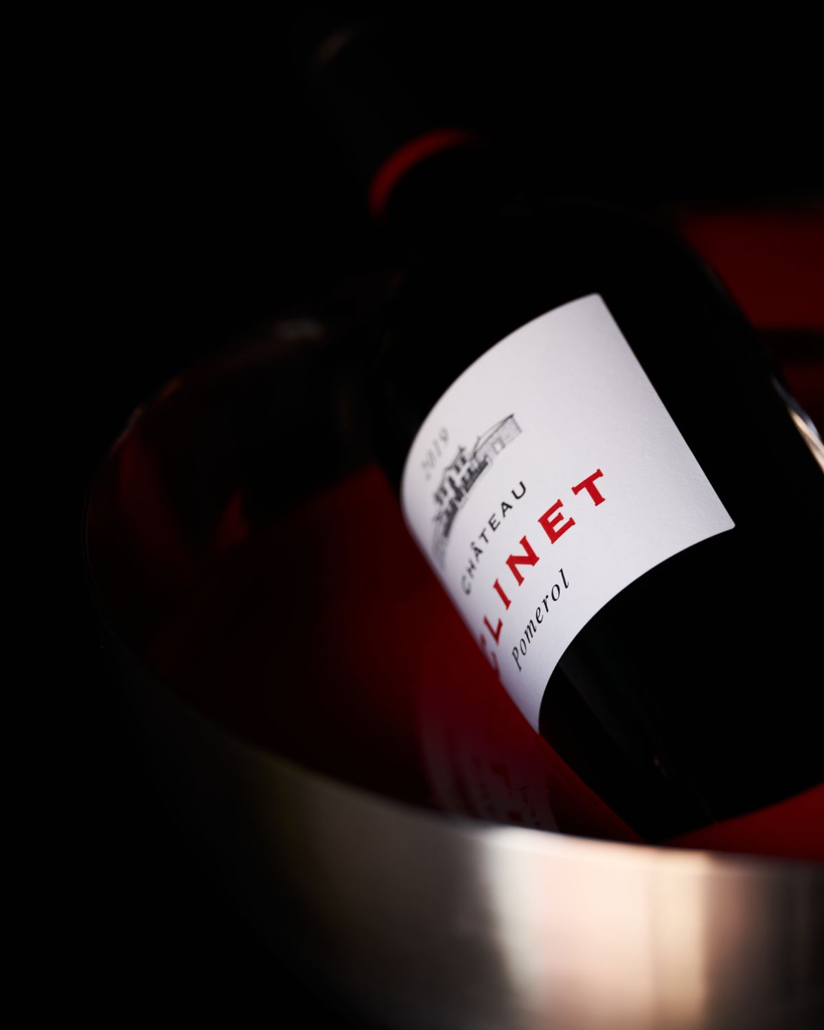 Bottle of Chateau Clinet sitting in a bucket of red paint, turned on its side.